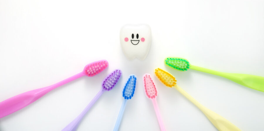 Aerial view of a rainbow of toothbrushes pointing toward a smiling tooth